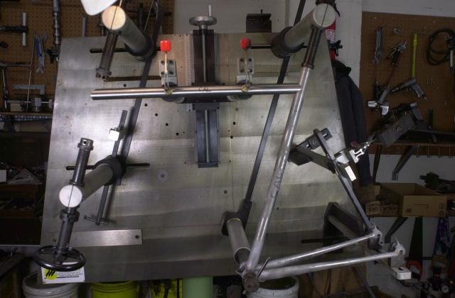 Previously the seat tube and chainstays of the next frame were tacked into the bottom bracket shell then removed from the fixture and completely brazed from the inside of the shell.  Now the frame returns to the fixture and the top tube, which has been mitred on both ends, is positioned.